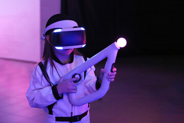 Little girl in virtual reality glasses holding an electric gun in her hands and in a white suit In a spacious room playing a 3D VR virtual reality computer game