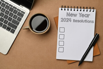 2024 New Year resolutions on a spiral notebook with coffee cup and laptop on table