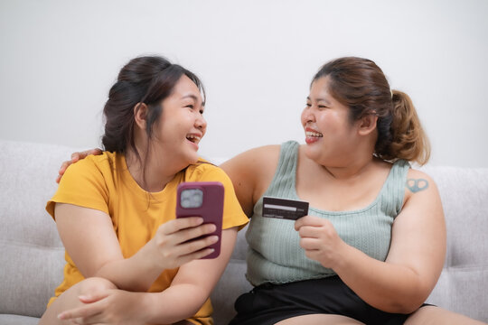 Two Asian over weight women do online shopping by smartphone and credit card at home with smile og happiness, appreciate emotion. Cozy life style at home.