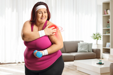 Fototapeta na wymiar Woman exercising at home and holding her painful red inflamed shoulder