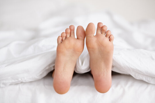 Bed, feet and person sleeping in home, relax and resting nap in sheets for health, calm and leisure in the morning. Foot, bedroom and closeup of toes in blankets, skin of legs and comfort in house