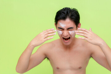 A young asian man screams after getting facial scrub cream into his eyes, irritating it. Isolated...