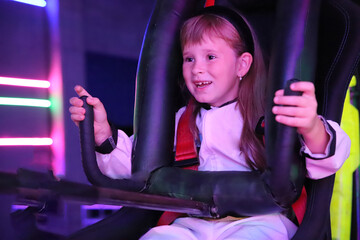 Adorable cheerful girl with long brown hair sits merrily on the attraction of virtual reality computer game in white suit