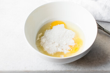 Egg and sugar in a white bowl, process of making cake or madeleines
