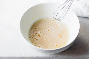 Eggs and sugar that has been whisked together in a white mixing bowl till pale and fluffy, Egg and sugar in a white bowl, process of making cake