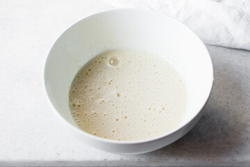 Eggs and sugar that has been whisked together in a white mixing bowl till pale and fluffy, Egg and sugar in a white bowl, process of making cake