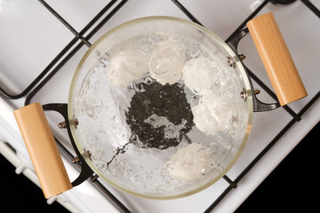 Top closeup view of transparent glass saucepan with boiling eggs on a gas stove