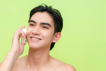A handsome young man smiles while rubbing a bar of mild white soap on his cheeks. Against a light...
