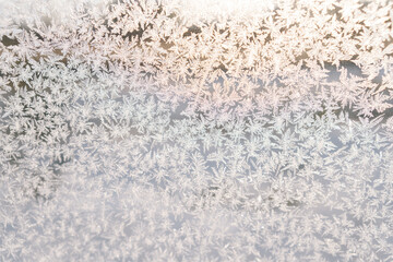 Closeup of beautiful texture on glass with frozen pattern on sunny winter day. Close-up of frosty natural pattern on window glass on background of soft sunlight. Concept of festive atmosphere.