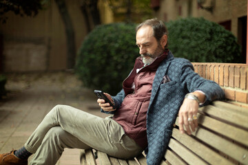 Retired senior man looking at his mobile phone sitting on a bench