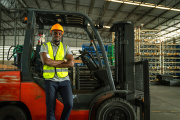 Happy African American male engineer driving and operating on a forklift truck in the industry factory. Man technicians wear safety helmets, and uniforms driving forklift truck