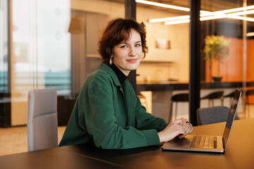 A businesswoman from Generation Z diligently works on her laptop in a flexible startup office. The...