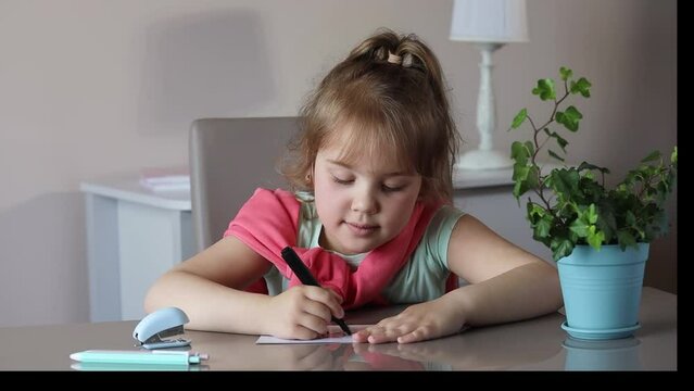Caucasian little child girl sitting at table and making home lessons.Smart lid concept. Home education.