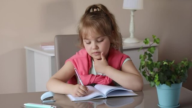 Caucasian child girl whriting on textbook sitting at table home.Kid learning. Little smart pupil do school home work, task resolving. 