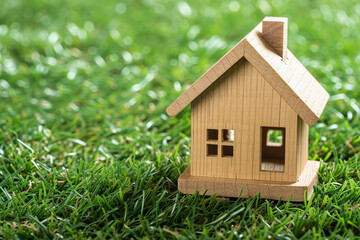 Small wooden house mockup on green grass, new home purchase and empty space for text