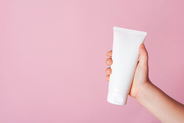 Child little hand holding white cream tube on pink background. Daily children beauty product....