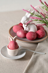 Traditional Easter holiday food and table setting decor, pink dyed eggs in egg cup and on plate, rabbit figurine, spring flowers bouquet, soft selective focus