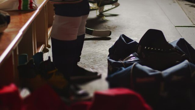 Ice Hockey player ties up laces on pants. Man wears protective equipment gear in locker room. Inside the checkroom, close up. Preparing for the game