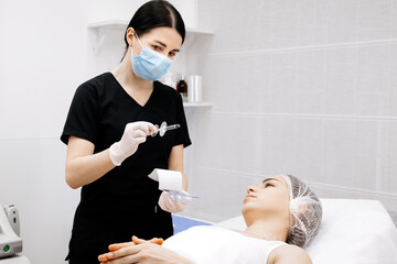 A female cosmetologist in gloves is preparing to give a young woman a cosmetological procedure....