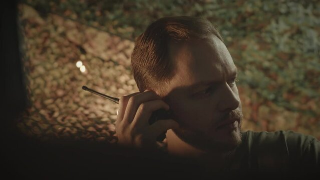 Chest up of young Caucasian military officer communicating with coworker via walkie talkie while working at night in military control center