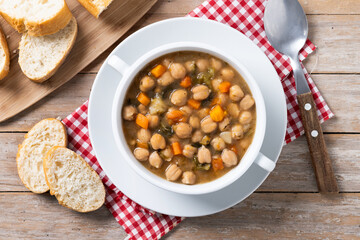 Chickpeas soup with vegetables in bowl on wooden table. Top view