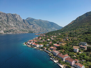 Fototapeta na wymiar Bird's eye view of a charming village of Prcanj along the azure waters of Kotor Bay, encircled by the lush mountains of Montenegro.