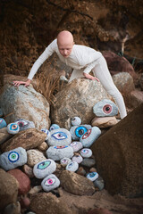 Young hairless girl with alopecia in white futuristic costume looking at surreal landscape with lot of rocks eyes, symbolizing connection between human spirit and earth