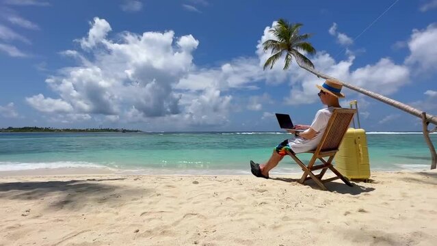 Nomad digital  young man with the laptop and running remotely with bright scenic view near poolside on the beach in summer time	