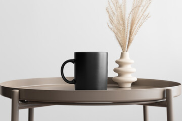 Black mug mockup with a reed pampas decoration on the beige table.