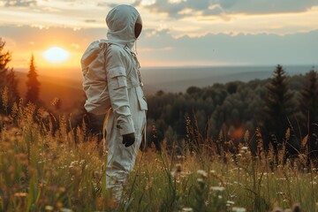 An astronaut in a full suit gazes at the sunset amidst a meadow, a forest backdrop behind them