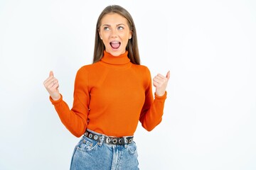 Ecstatic young beautiful caucasian woman wearing orange turtleneck shout loud yeah fist up raise...