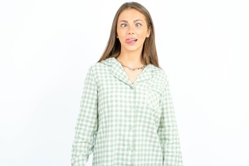 Funny Beautiful young woman wearing green plaid pyjama makes grimace and crosses eyes plays fool...