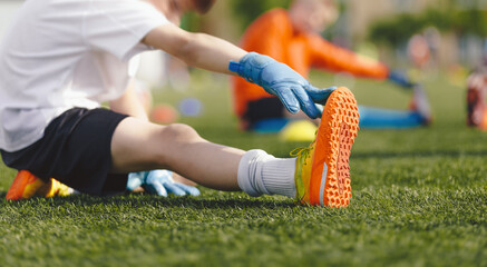 Young Boy Doing Soccer Stretching Exercises. Kids in Football Goalkeepers Training. Group of School Boys in Soccer Goalie Practice During Summer Time. Youth players in Soccer Gloves and Cleats