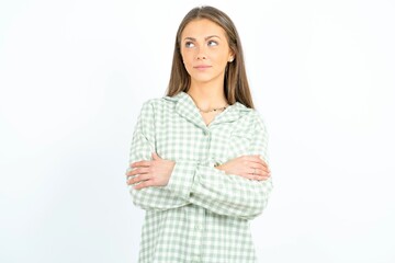Charming thoughtful Beautiful young woman wearing green plaid pyjama stands with arms folded concentrated somewhere with pensive expression thinks what to do