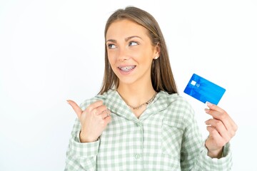 Beautiful young woman wearing green plaid pyjama hold credit card point empty space