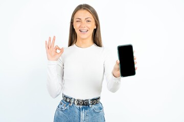 Young beautiful woman holding in hands cell showing ok-sign