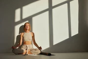 Fototapete Woman practicing yoga and meditation in lotus pose on yoga mat, relaxed. Mindful meditation concept. Wellbeing © MaxFrost