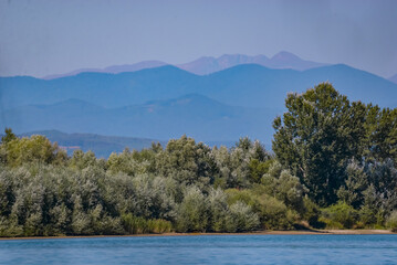 Summer landscape with a blue lake and mountains in the background. Green forest at the edge of the water at the foot of the Carpathians