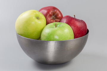 Apples different colors in bowl on gray background, side view