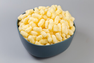 Sweet corn puffs in plastic kitchen bowl on gray background