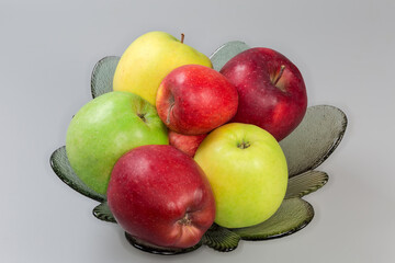 Apples different colors on glass fruit bowl on gray background