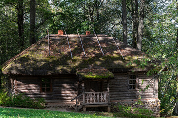 Old log bathhouse with a thatched roof and wooden porch stands on a slant in the woods, not far from the river.