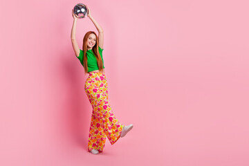Full size photo of positive cheerful girl wear stylish top print pants holding disco ball over head...