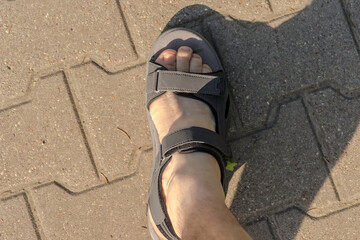 Męska stopa w sandale . Letni spacer w słoneczne popołudnie po brukowanym chodniku.  - obrazy, fototapety, plakaty