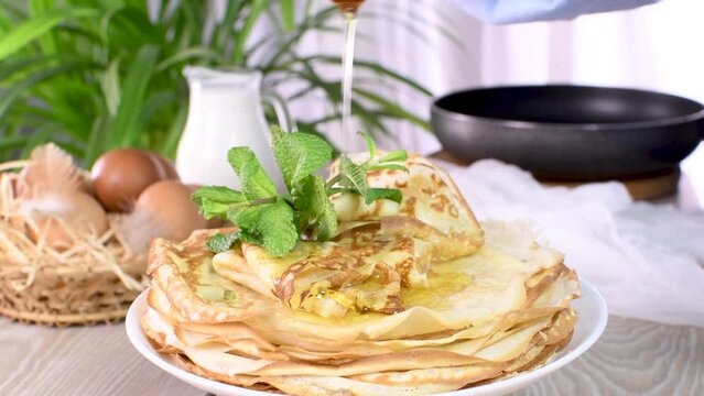 Freshly baked homemade thin pancakes with mint on a plate, season with honey. One of a series of video recipes. circle of rotation, close-up, slow motion