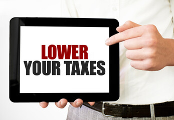 Text LOWER YOUR TAXES on tablet display in businessman hands on the white background. Business...