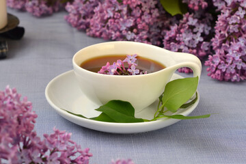 cup with black tea close-up and lilac flowers nearby