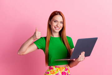 Photo of charming satisfied woman with ginger hairdo dressed green t-shirt show thumb up hold laptop isolated on pink color background