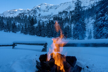Cozy fireplace with a burning wood fire at a snowy winter landscape with forest and mountains in...