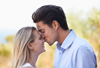 Naklejka premium Happy couple, kiss and nature for romance, support or affection in outdoor bonding or date. Young man kissing woman on nose with smile for embrace, comfort or love in forest or woods outside together